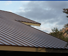 A close-up view of a house’s brown metal roof with overlapping panels, set against a cloudy sky and partially visible tree branches—showcasing Prime Roofing and Restoration’s expert roofing services in Georgia.