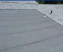 A close-up view of a roof in Georgia with gray asphalt roll roofing in the foreground and overlapping shingle roofing in the background, two small vent pipes visible—quality work by Prime Roofing and Restoration's expert roofing services.