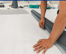 A person’s hands cutting a large sheet of white flooring material with a utility knife, next to a roll of similar material and some tools in the background, showcasing Prime Roofing and Restoration's expert services in Georgia.